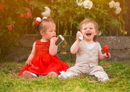 Little boy and girl playing with cellphones in the gardenの写真素材