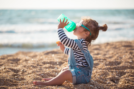 Little girl drinking water  on the beachの写真素材
