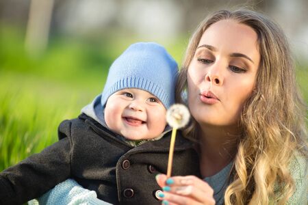 Mother with baby son on the meadow playing with dandelion flowerの写真素材