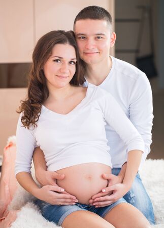 Man and pregnant woman portrait at homeの写真素材