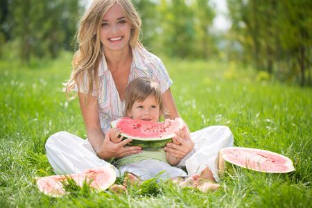 Happy mom and son eating watermelon on green grassの写真素材