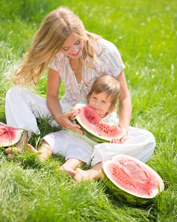 Happy mom and son eating watermelon on green grassの写真素材