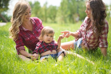 Happy two sisters with little boy laying on grass. Family picnic in spring parkの写真素材