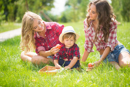 Happy two sisters with little boy laying on grass. Family picnic in spring parkの写真素材