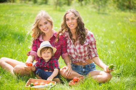Happy two sisters with little boy laying on grass. Family picnic in spring parkの写真素材