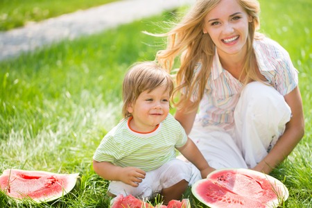 Happy mom and son eating watermelon on green grassの写真素材