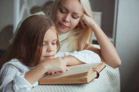 Mother with daughter reading book at homeの写真素材