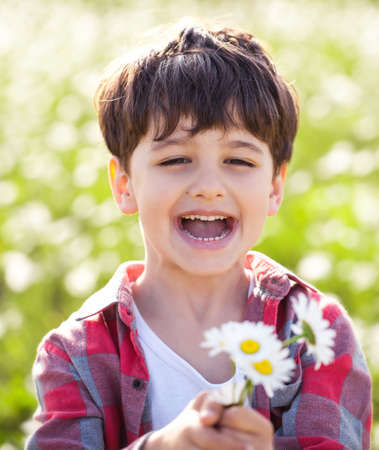 Little boy on the camomile meadow with flower in handの写真素材