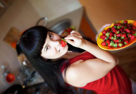 Brunette girl on the kitchen with plate of strawberryの写真素材