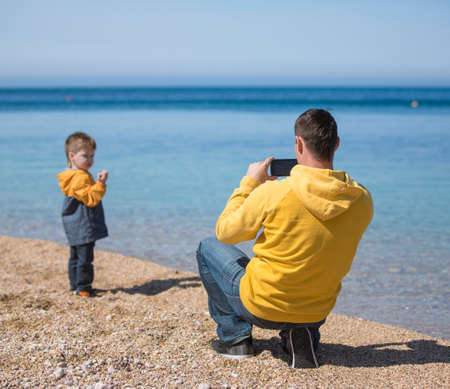 Father photographing his son on the beach at the day time. Concept of friendly family.の写真素材