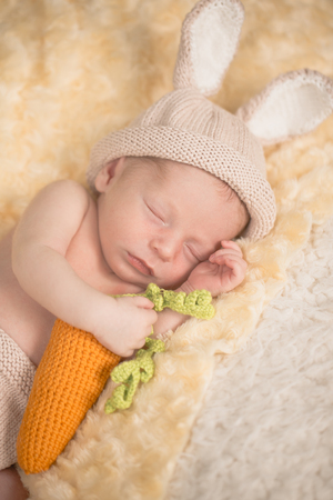 A precious newborn baby in rabbit costume with carrot is laying on a bed, sleeping peacefully.の写真素材
