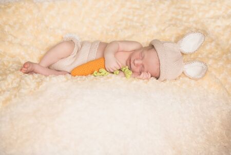 A precious newborn baby in rabbit costume with carrot is laying on a bed, sleeping peacefully.の写真素材