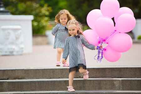 Happy little girls playing on the street with pink balloons.の写真素材