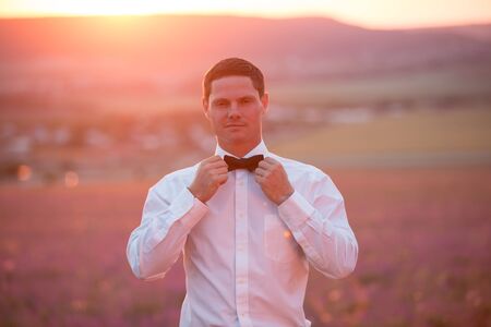 Elegant young guy posing on lavender field at sunset timeの写真素材
