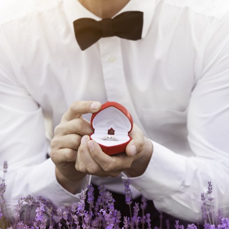 Elegant young man proposing with an engagement ring at lavender field with the focus on the ringの写真素材