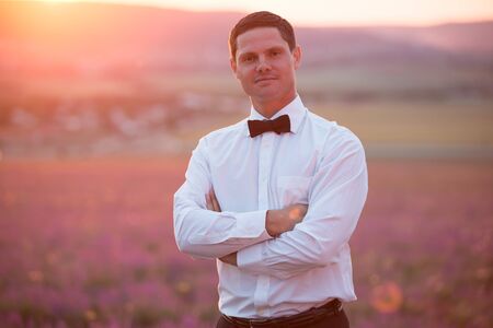 Elegant young guy posing on lavender field at sunset timeの写真素材