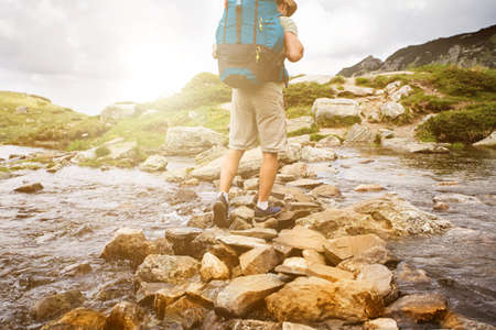 Hiker man with backpack crossing a river on stones in bulgarian mountains. Hiking and leisure theme....