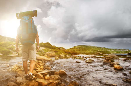 Hiker man with backpack crossing a river on stones in bulgarian mountains. Hiking and leisure theme....