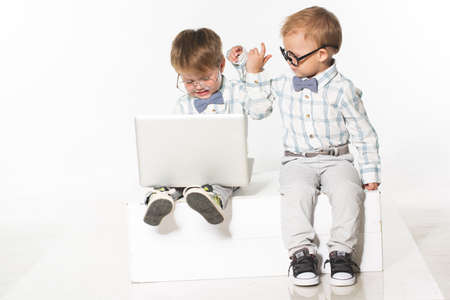 Two cute baby in business clothes with the glasses on the eyes with a laptop. Isolate photo in studio.の写真素材