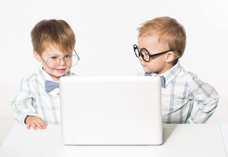 Two cute baby in business clothes with the glasses on the eyes with a laptop. Isolate photo in studio.の写真素材