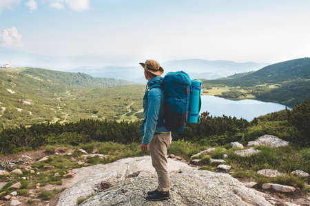 Young man with backpack standing on the mountain and enjoying valley viewの写真素材