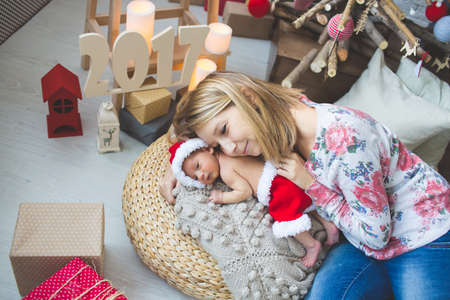 Portrait of young mom and her sleeping newborn baby boy in Santa clothesの写真素材