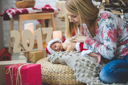 Portrait of young mom and her sleeping newborn baby boy in Santa clothes