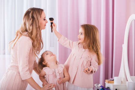 Mother and two daughters doing lip make-up.の写真素材
