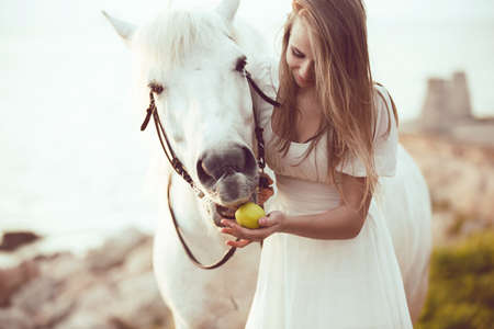 Girl in white dress with horse on the beachの写真素材