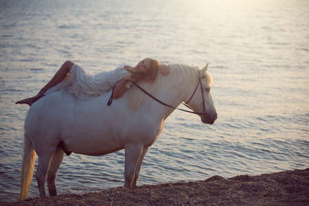 Girl in white dress with horse on the beachの写真素材