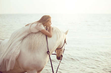 Girl in white dress with horse on the beachの写真素材