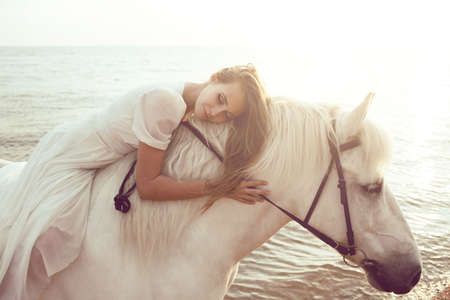 Girl in white dress with horse on the beachの写真素材