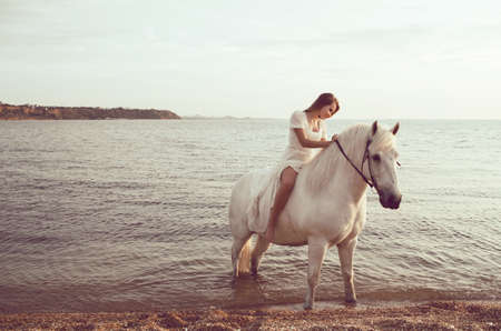 Girl in white dress with horse on the beachの写真素材