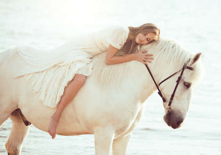 Girl in white dress with horse on the beach