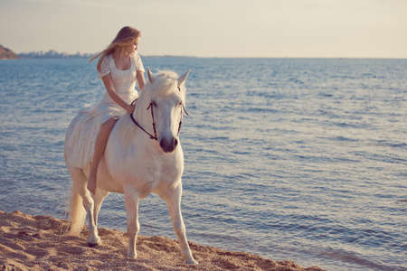 Girl in white dress with horse on the beachの写真素材