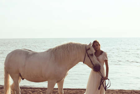 Girl in white dress with horse on the beachの写真素材