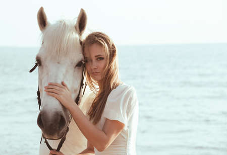 Girl in white dress with horse on the beachの写真素材