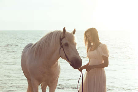 Girl in white dress with horse on the beachの写真素材