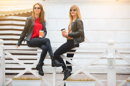 Portrait of two beautiful young girlfriends with paper cups of coffee in hands.の写真素材