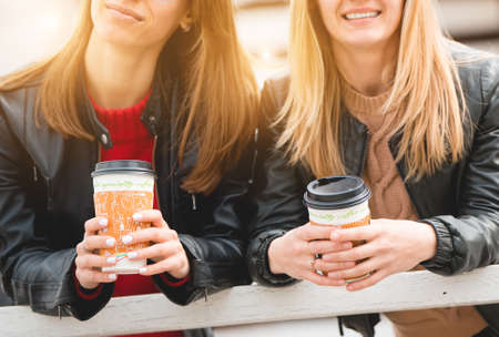 Portrait of two beautiful young girlfriends with paper cups of coffee in hands.