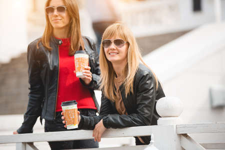 Portrait of two beautiful young girlfriends with paper cups of coffee in hands.の写真素材