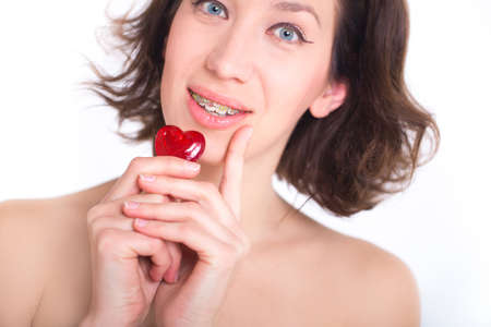 Beautiful girl with perfect skin and multi-colored braces posing with small heart in handsの写真素材