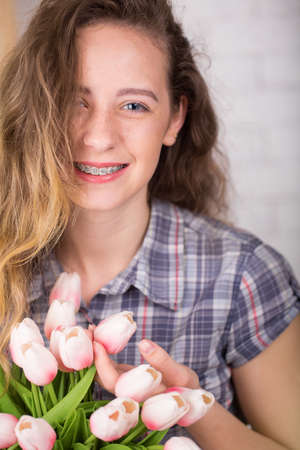 A teenage girl smiles with birches. Posing against a brick wall background with a bouquet of tulips.の写真素材