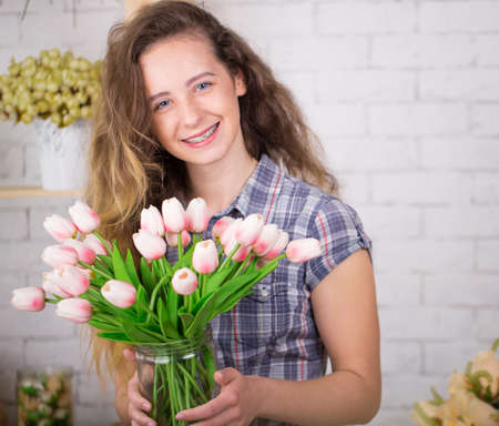 A teenage girl smiles with birches. Posing against a brick wall background with a bouquet of tulips.の写真素材