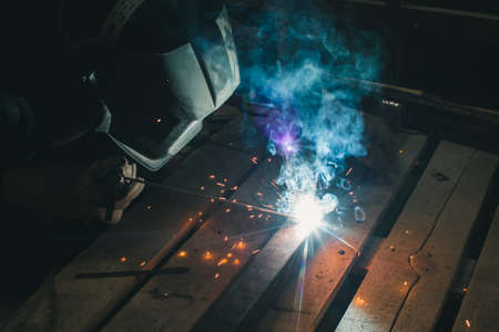 Worker with personal protective equipment and protective mask welding steel pipe in factory.の写真素材