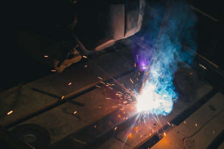Worker with personal protective equipment and protective mask welding steel pipe in factory.の写真素材