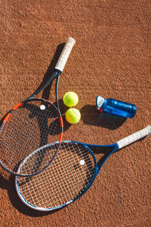 Tennis balls, rackets and bottle of water on the clay courtの写真素材