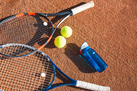 Tennis balls, rackets and bottle of water on the clay courtの写真素材