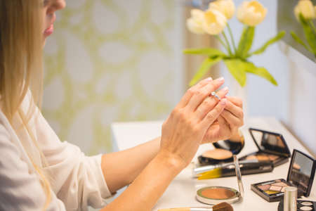 Portrait of young beautiful blonde hair woman sitting near dressing table and doing makeup at home.の写真素材