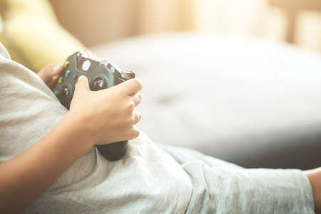 Close up of child hands holding a joystick controller while playing a video games at home.の写真素材